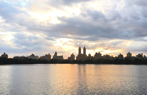 Photo of sun setting across Kennedy Lake in Central Park with buildings in the background.